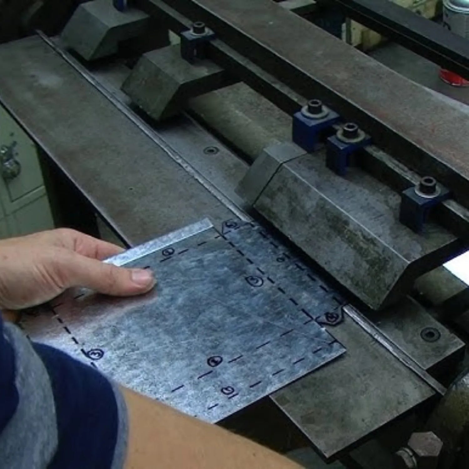 Person holding a metal sheet next to a machine in a workshop setting